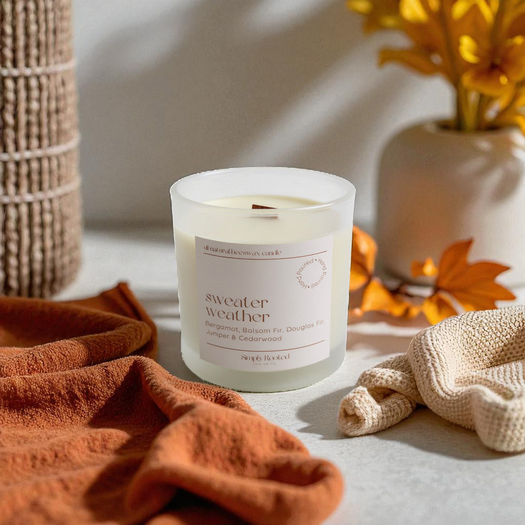 Candle labeled 'sweater weather' on a surface with autumn-themed decor