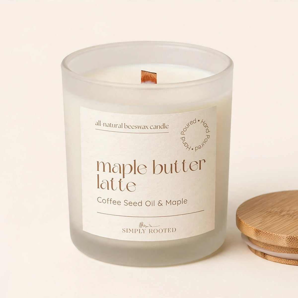 A frosted glass jar candle labeled 'maple butter latte' with a small wooden wick, shown next to a round bamboo lid on a warm off-white background. The brand 'Simply Rooted' is visible on the label.
