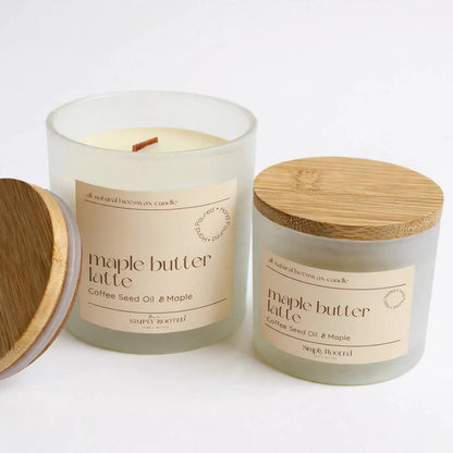 Two soy candles in frosted glass jars with light wood lids, shown on a clean white background. One jar is open with its lid leaning beside it, revealing cream-colored wax and a wick, while the other jar is closed with its bamboo-style lid on top.
